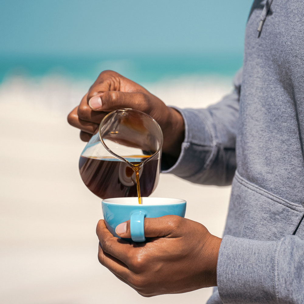man pouring freshly roasted Iwacu coffee at the beach